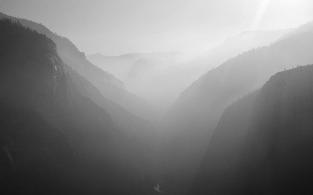 Black-and-white landscape photo of wide valley with mist.
